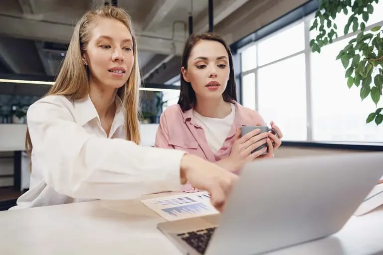 Una manager guida una collaboratrice davanti al pc, rappresentazione di come il ruolo manageriale significhi supportare il team e non sia solo un titolo.
