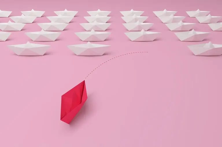 Una barchetta di carta rosa naviga in testa a un gruppo di barchette bianche, metafora di un leader che guida e influenza positivamente il proprio team.